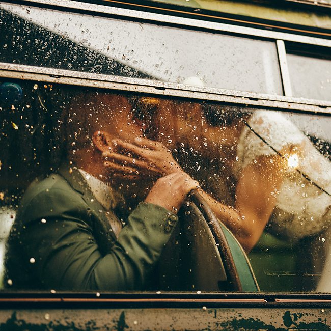 Les mariés s’embrassent derrière une vitre mouillée